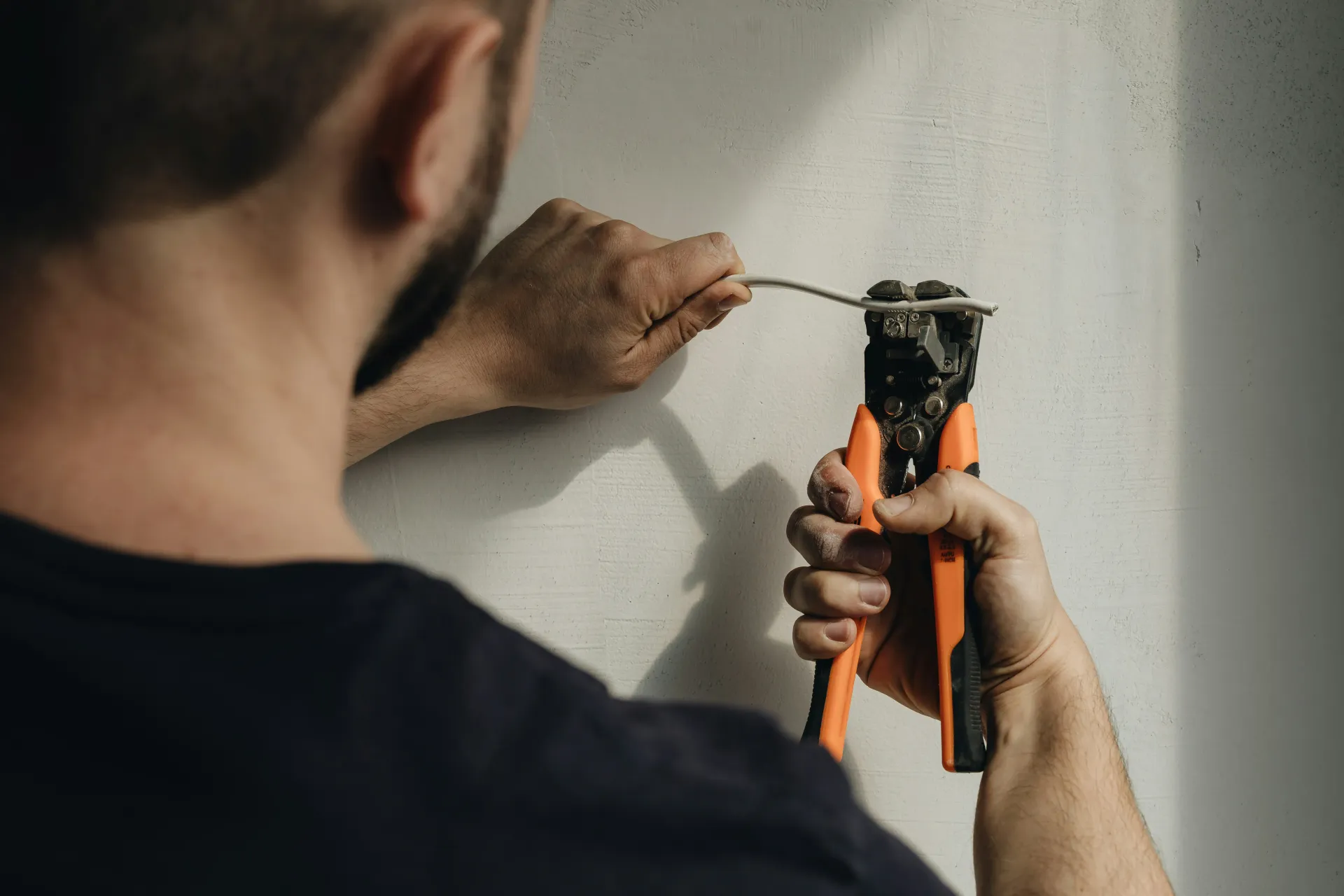 Electrician stripping a white electrical wire with orange wire strippers.