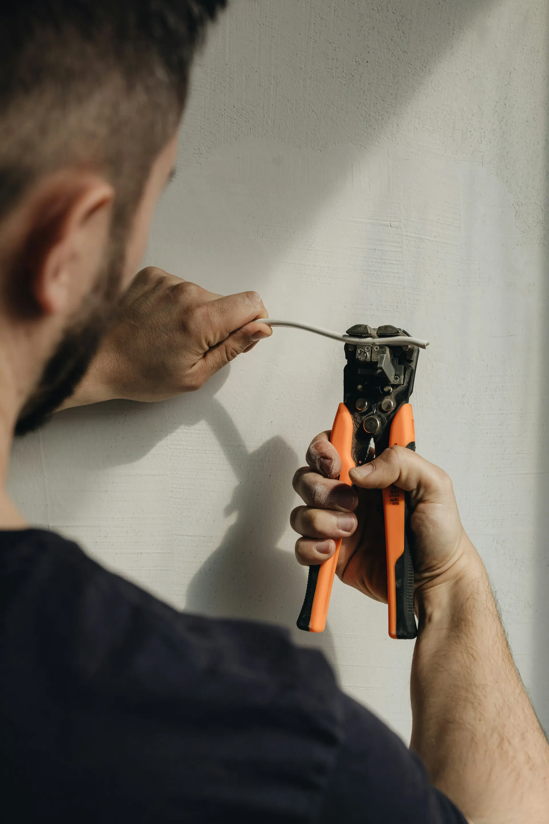 Electrician stripping an electrical wire with a professional tool.