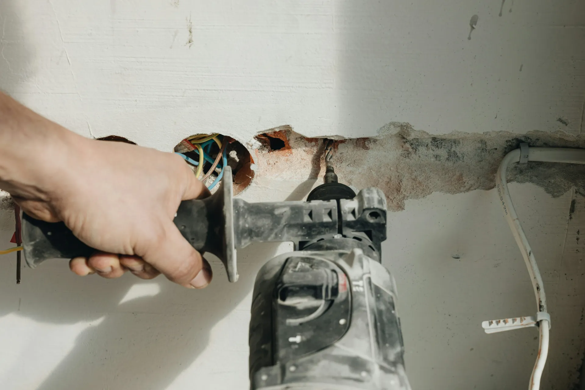Electrician drilling into a wall during an electrical installation or rewire project.